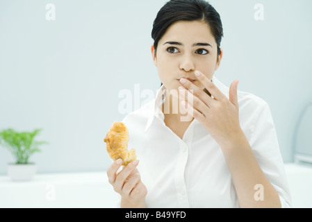 Junge Frau mit Croissant, andere Hand vor Mund Stockfoto