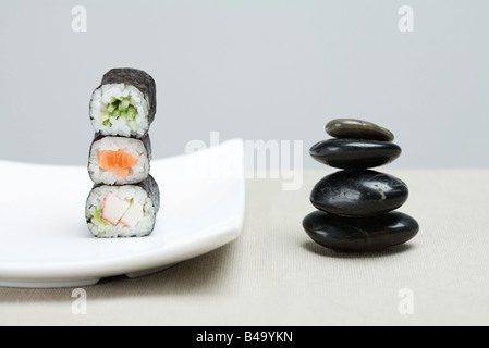 Stapel von drei Stücken Maki Sushi neben Stapel von glänzenden schwarzen Kieseln platziert Stockfoto