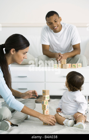 Mutter und Kleinkind Mädchen spielen mit Bausteinen, Tochter über Schulter Vater im Hintergrund Stockfoto