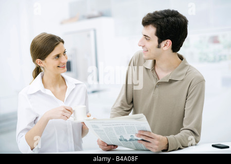 Paar lächelnd an einander, Mann mit Zeitung, Frau mit Kaffeetasse Stockfoto