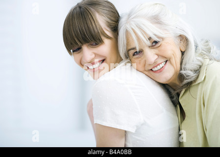 Ältere Frau lehnte sich gegen Erwachsene Tochter zurück, lächelt in die Kamera Stockfoto