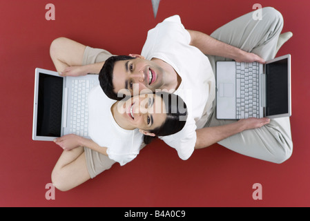 Paar sitzen Rücken an Rücken auf dem Boden halten Laptops, lächelte Kamera Stockfoto