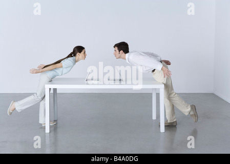 Mann und Frau an den entgegengesetzten Enden des Tisches, Neigung zu einander, Laptop-Computer zwischen Ihnen Stockfoto