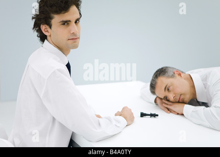 Junger Geschäftsmann über Tisch von besiegt älteren Geschäftsmann, Schachfigur zwischen ihnen sitzen Stockfoto
