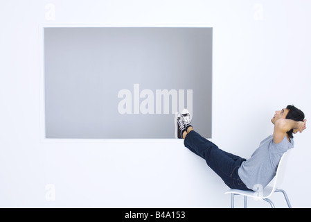 Mann sitzt im Stuhl mit Händen hinter dem Kopf und Beine hoch, Blick nach oben Stockfoto