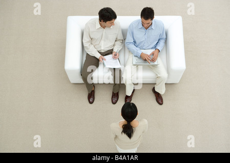 Berufstätige Männer auf Sofa sitzen, diskutieren Dokument, Frau stand vor ihnen, Overhead anzeigen Stockfoto