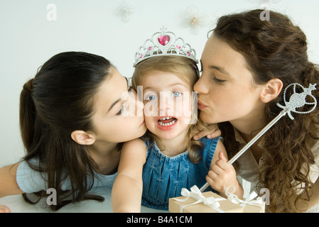 Kleines Mädchen verkleidet als Prinzessin, wird von Mutter und Schwester auf Wangen geküsst Stockfoto