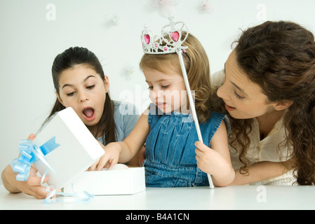 Kleines Mädchen öffnen, Geburtstagsgeschenk, Mutter und Schwester beobachten Stockfoto