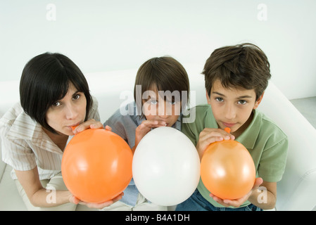 Mutter und zwei Söhne aufblasen Luftballons, Blick in die Kamera, erhöhte Ansicht Stockfoto
