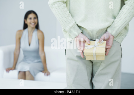 Mann hält Geschenk hinter seinem Rücken, im Hintergrund, lächelnde Frau beschnitten Ansicht Stockfoto