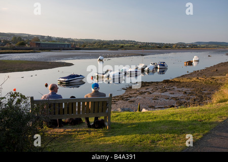 Zwei Männer mit Hunden sitzen auf einer Bank neben der Axt-Mündung im Abendlicht, Axmouth, East Devon Stockfoto