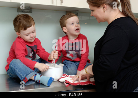 Mama und Zwillinge dreieinhalb Jahre alt sitzen auf Küche Bench Top einige Backen zu tun Stockfoto