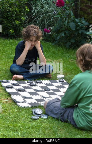 Zwei Jungs sitzen auf dem Rasen im Garten auf einem überdimensionalen Schachbrett Schach spielen Stockfoto
