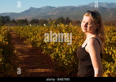 Schöne blonde Frau stand mit geschlossenen Augen in der untergehenden Sonne in einem herbstlichen Weinberg Stockfoto