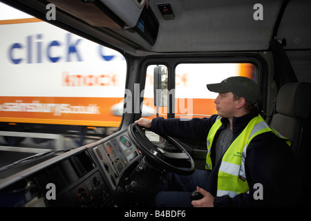 Tragen eines High-Vis Wappenrock und Schirmmütze, sitzt ein junger Fahrer am Steuer von seinem LKW-LKW auf der A3-Stamm-Straße in London