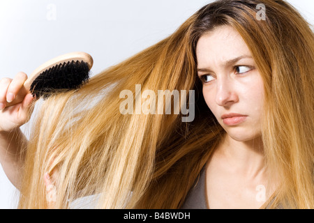 Junge Frau mit Haarbürste besorgt an den wirren Haaren Stockfoto