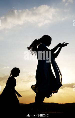 Zwei indische Schwestern Durchführung einer hinduistischen frommen Tanzes auf einem Felsen bei Sonnenuntergang Silhouette. Andhra Pradesh, Indien Stockfoto