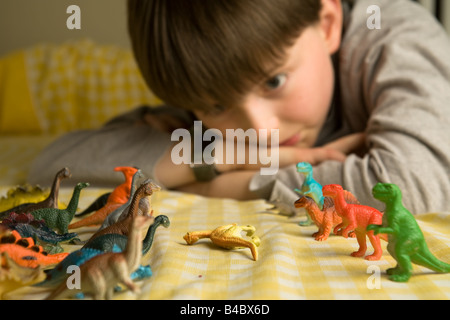 Ein pre-teen junge blickt über eine Horde von bunten Spielzeug Dinosaurier organisiert in Schlacht Reihen mit einem gefällten Diplodocus zwischen Ihnen Stockfoto