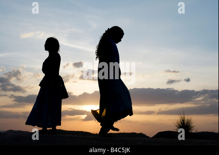 Zwei indische Schwestern tanzen auf einem Felsen bei Sonnenuntergang Silhouette. Andhra Pradesh, Indien Stockfoto