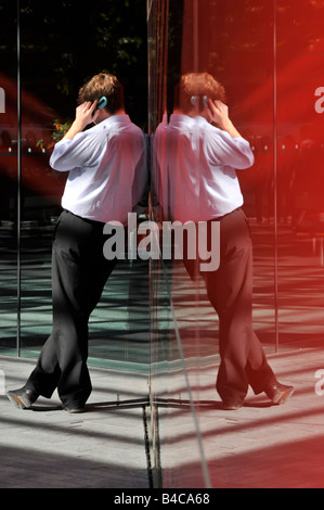 Junger Bursche sprechen auf Handy gelehnt Glas Wand Büro Verkleidung zur Mittagszeit Stockfoto