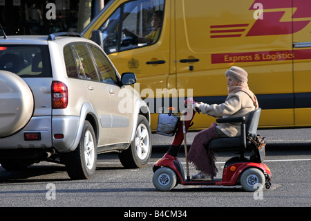 Ältere Person, die fährt Roller Mobilität zwischen Verkehr und geparkte Fahrzeuge Stockfoto