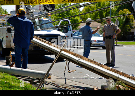 Elektriker und ein Polizist diskutieren die Situation der zerstörten Strommast nach ein SUV durch sie stürzte Stockfoto