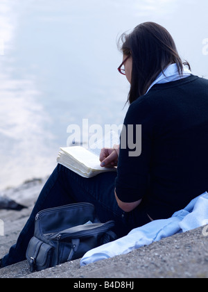 Junge Frau mit Brille setzte auf Stufen hinunter zum Wasser, ein Buch zu lesen Stockfoto