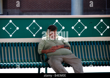 Ein obdachloser Mann schläft auf einer Bank in der noontime Sonne in Oklahoma City, Oklahoma, USA. Stockfoto