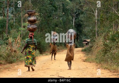 Frau und Kinder mit tontöpfen auf Kopf über unbefestigte Straße, Burundi, Afrika Stockfoto