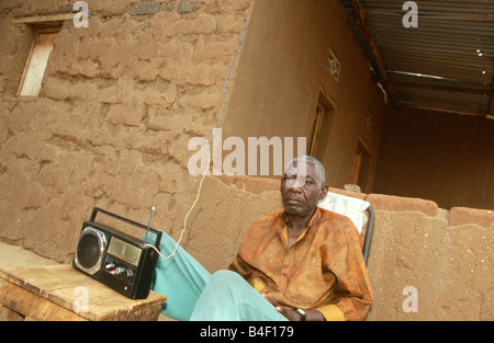 Ältere Mann sitzt vor dem Haus Radio hören, Burundi, Afrika Stockfoto