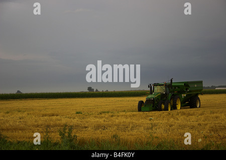 Ein John Deere Traktor und ein Getreide Wagen sitzen in einem abgeernteten Weizenfeld, wie ein Sturm bewegt sich. Stockfoto