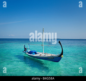 Ein Fischer entspannt auf seinem traditionellen maledivischen Fischerboot, während es auf tropischen Wasser Aqua blaue Wasser schwimmt. Stockfoto