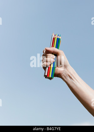 Eine menschliche Hand halten eine Handvoll Buntstifte vor blauem Himmel Stockfoto