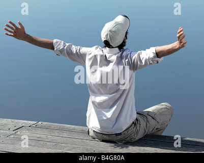 Ein junger Mann sitzt auf einem Steg mit seine Arme ausgestreckt Stockfoto