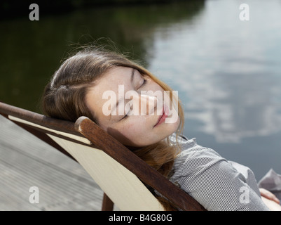 Eine junge Frau sitzt in einem Liegestuhl, schloss die Augen Stockfoto