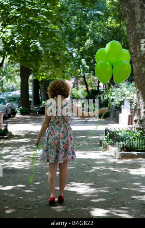 Eine junge Frau zu Fuß eine Stadt Gehweg mit Luftballons, Rückansicht Stockfoto