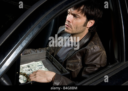 Ein Mann sitzt in einem Auto mit einer offenen Aktentasche voller Geld Stockfoto