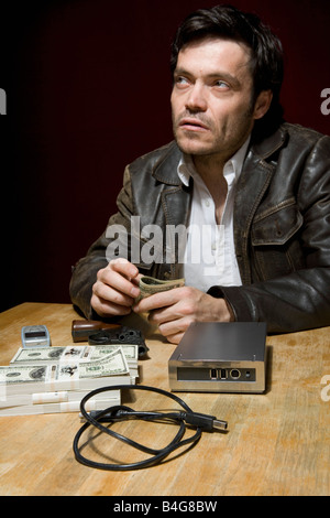 Ein Mann sitzt an einem Tisch mit Stapeln von Geld, ein Handy und eine Festplatte Stockfoto
