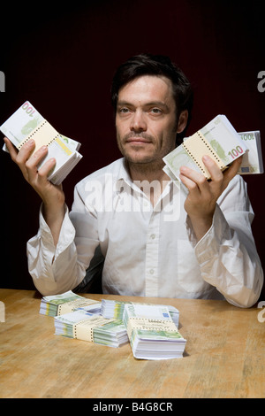 Ein Mann sitzt an einem Tisch mit Bündeln von hundert Euro-Banknoten Stockfoto