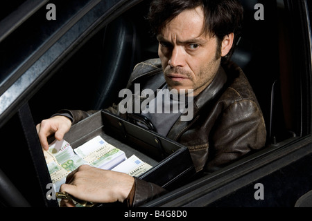 Ein Mann sitzt in einem Auto mit einer offenen Aktentasche voller Geld Stockfoto