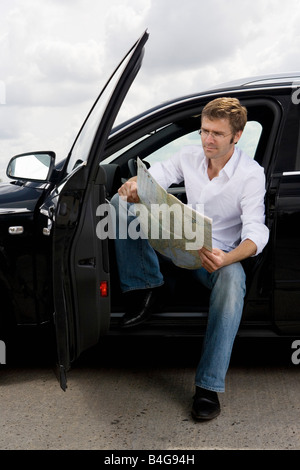 Ein Mann sitzt in einem Auto bei geöffneter Tür und Kartenlesen Stockfoto