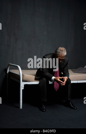 Ein Business-Mann sitzt auf einem Gefängnis-Zelle-Bett Stockfoto