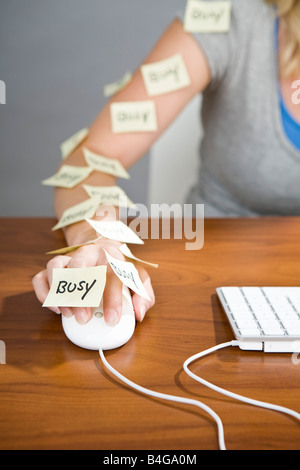 Ein menschlicher Arm mit einer Computermaus mit Haftnotizen drauf, bei denen das Wort beschäftigt geschrieben auf Sie Stockfoto