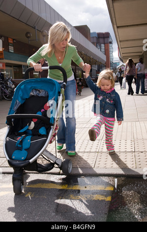 Mutter, die zu Fuß in ein Einkaufszentrum hielt ihre Tochter s Hand und schob einen buggy Stockfoto