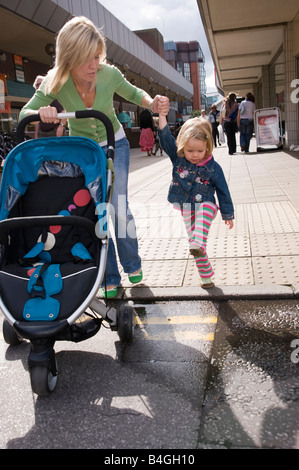 Mutter, die zu Fuß in ein Einkaufszentrum hielt ihre Tochter s Hand und schob einen buggy Stockfoto