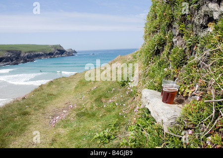 Zwei Pints Bier sitzen auf einer Schiefertafel Bank auf dem kornischen Küstenpfad mit Himmel und Surfer im Hintergrund Crantock cornwall Stockfoto