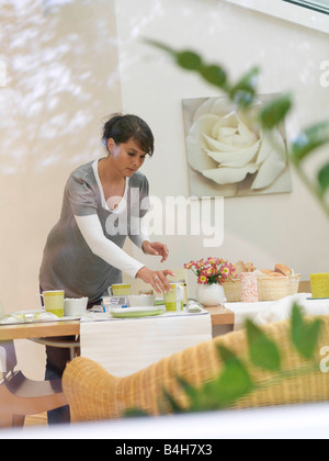 Junge Frau, die Frühstück am Tisch platzieren Stockfoto