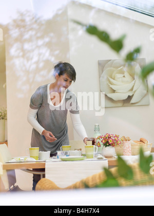 Junge Frau, die Frühstück am Tisch platzieren Stockfoto