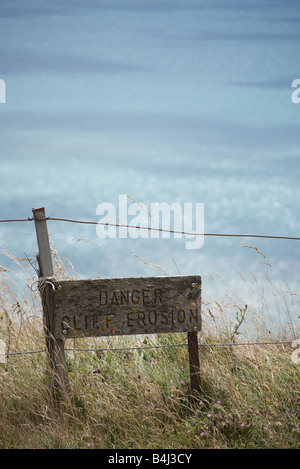 Ein Warnsignal, das besagt "Cliff Edge" Beach Head, East Sussex, England mit einem blauen Meer und Himmel dahinter. Stockfoto