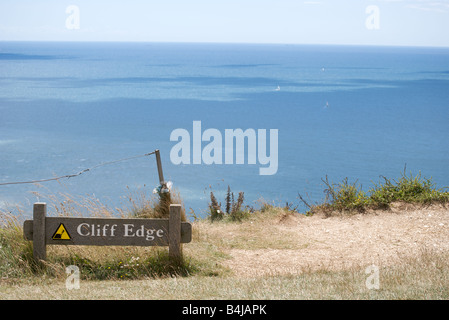 Ein Warnsignal, das besagt "Cliff Edge" Beach Head, East Sussex, England mit einem blauen Meer und Himmel dahinter. Stockfoto